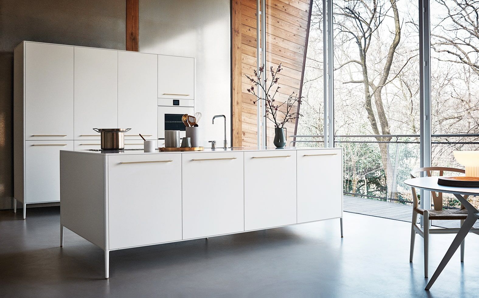 Cuisine moderne blanche avec vue sur la forêt et accessoires de cuisine dorés.